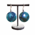 A pair of round drop earrings with a marbled blue and teal pattern, hanging from silver hooks on a black jewelry display stand against a white background.