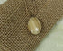 A natural wood oval pendant necklace with a gold-toned chain, displayed on a textured burlap surface.