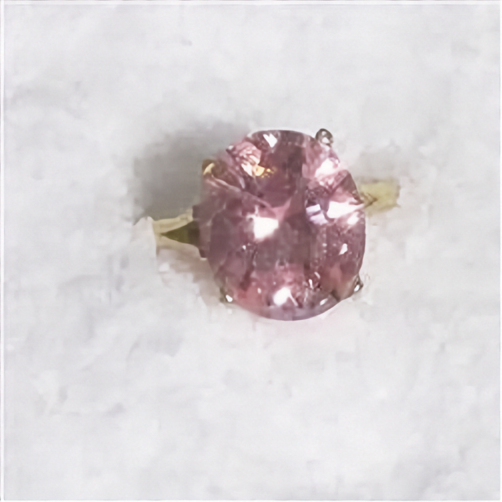 An oval-cut pink gemstone ring set in a yellow gold band, photographed on a textured white background.