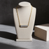 A gold chain necklace with a rectangular silver-toned bar pendant displayed on a cream jewelry bust against a dark gray background.